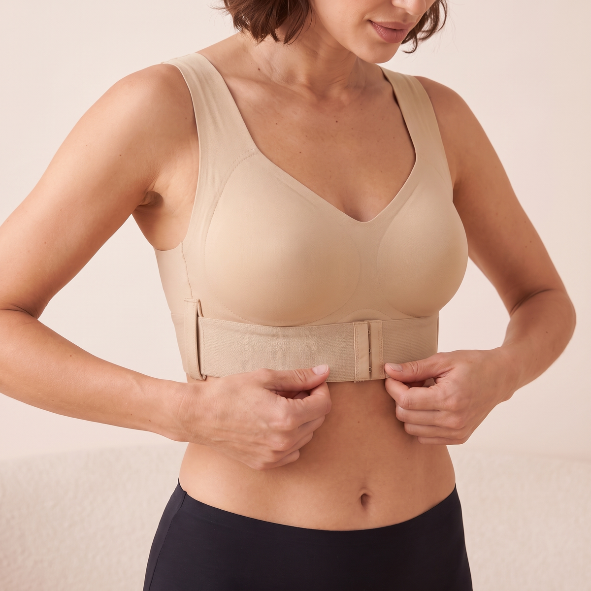 Soutien-gorge MUE beige porté par un mannequin adulte à la silhouette menue, mains en cours de réglage de la bande à l’avant — visuel généré.