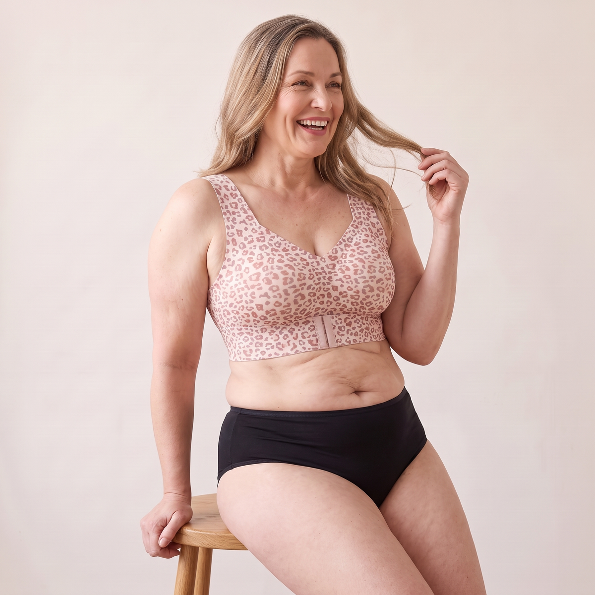 Soutien-gorge MUE léopard clair porté par un mannequin adulte d’environ 48 ans à la silhouette généreuse, assis de côté sur un tabouret, bras levé — visuel généré.