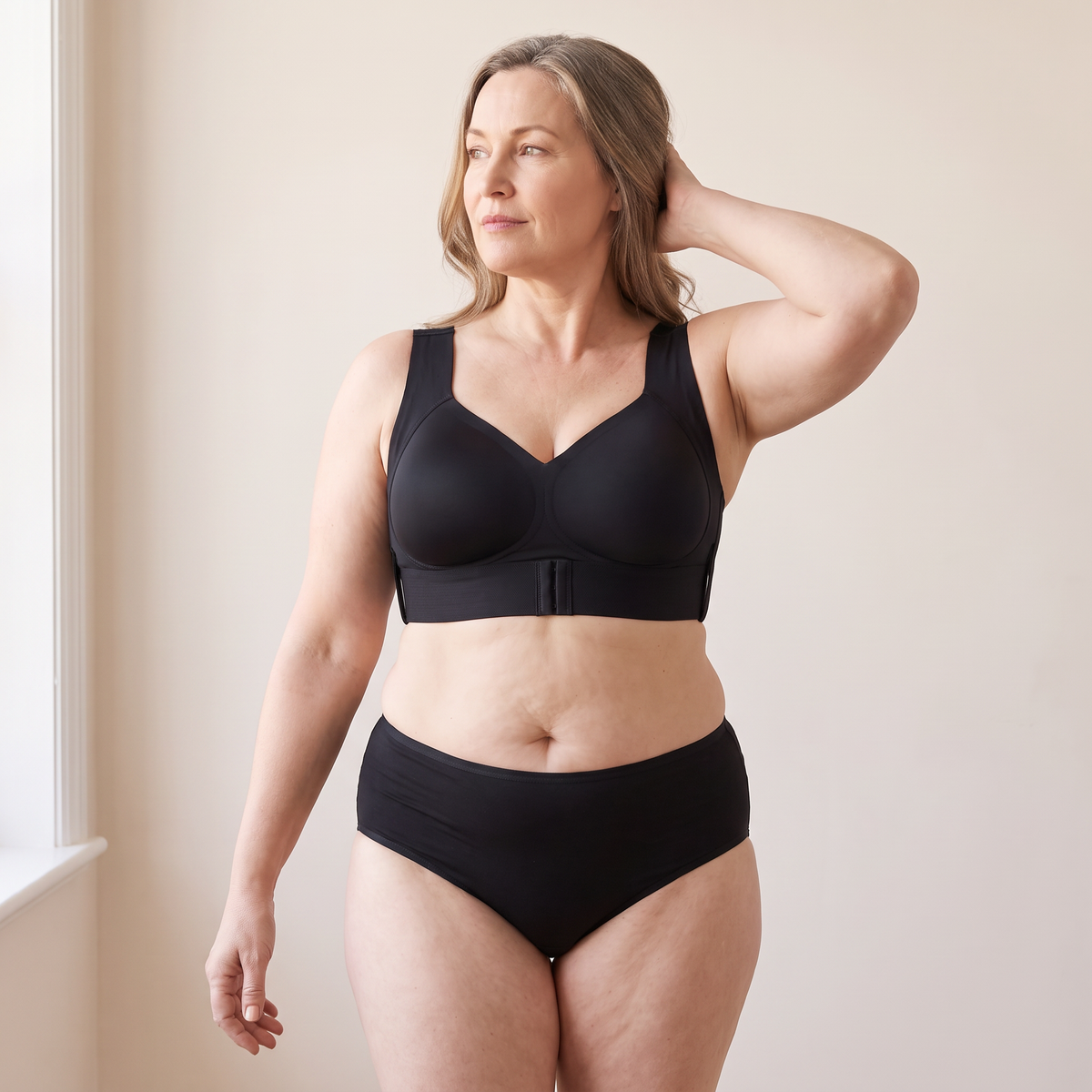 Soutien-gorge MUE noir porté par un mannequin adulte d’environ 48 ans à la silhouette généreuse, bras levé dans les cheveux et regard de côté — visuel généré.
